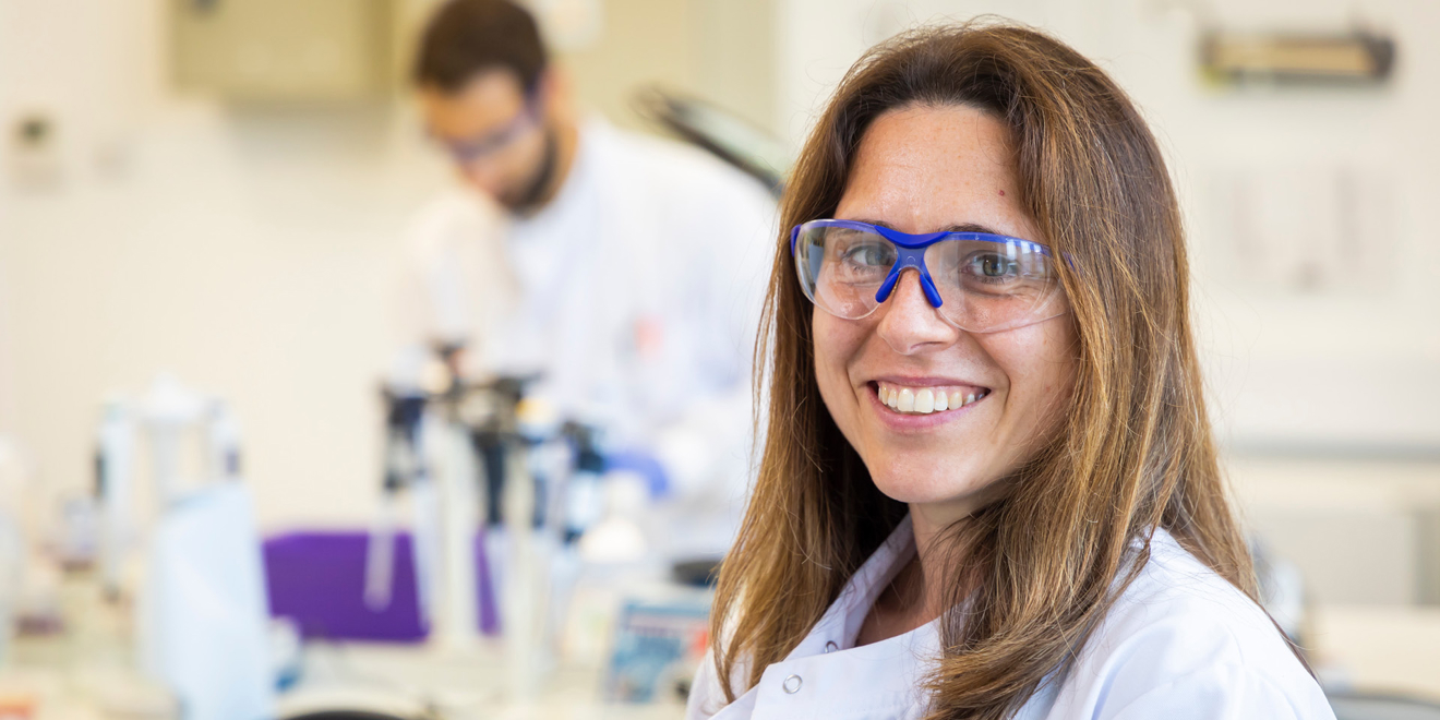 Woman in labcoat and protective goggles smiling