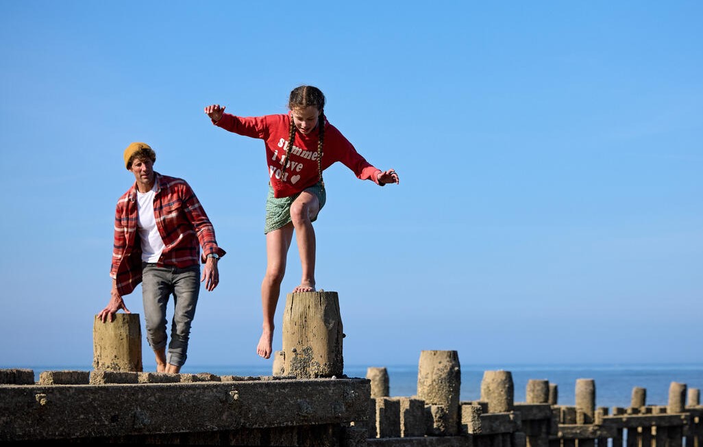 Adult man and 10-year-old girl climb on the pier by the beach in Norfolk.