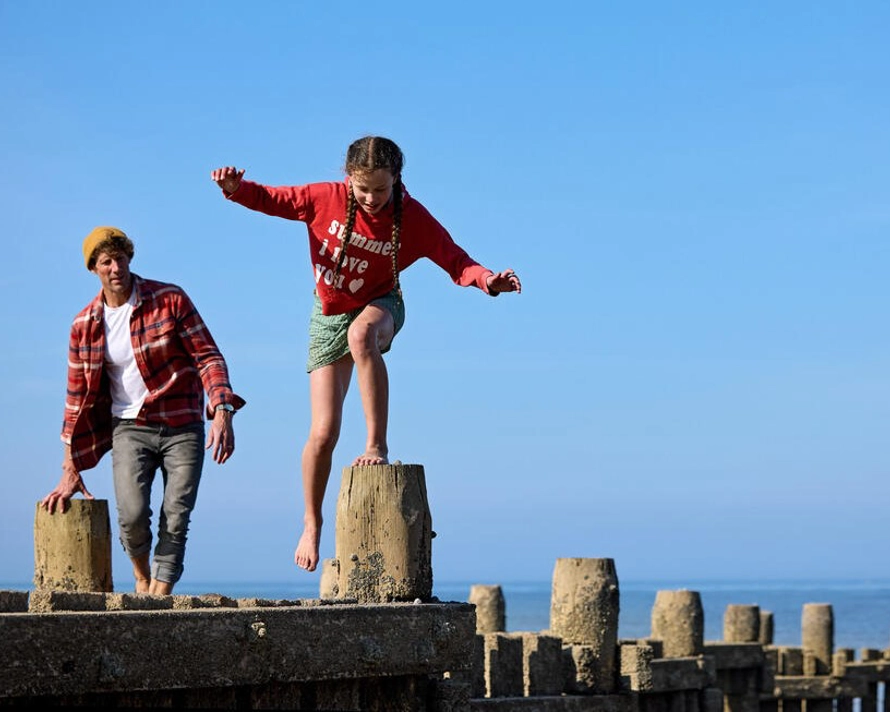 Adult man and 10-year-old girl climb on the pier by the beach in Norfolk.