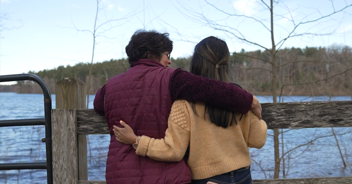 Two women with their arms around each other looking out at water