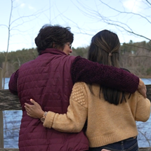 Two women with their arms around each other looking out at water