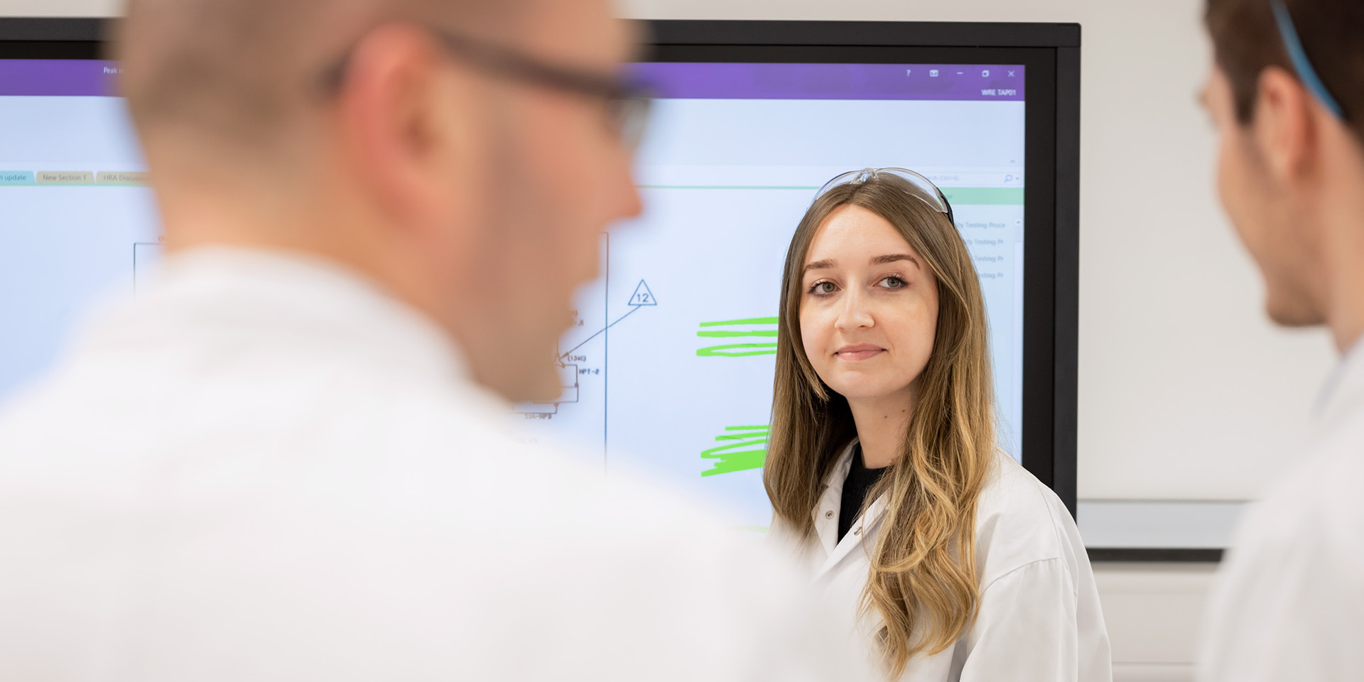Three employees in labcoats and goggles laughing