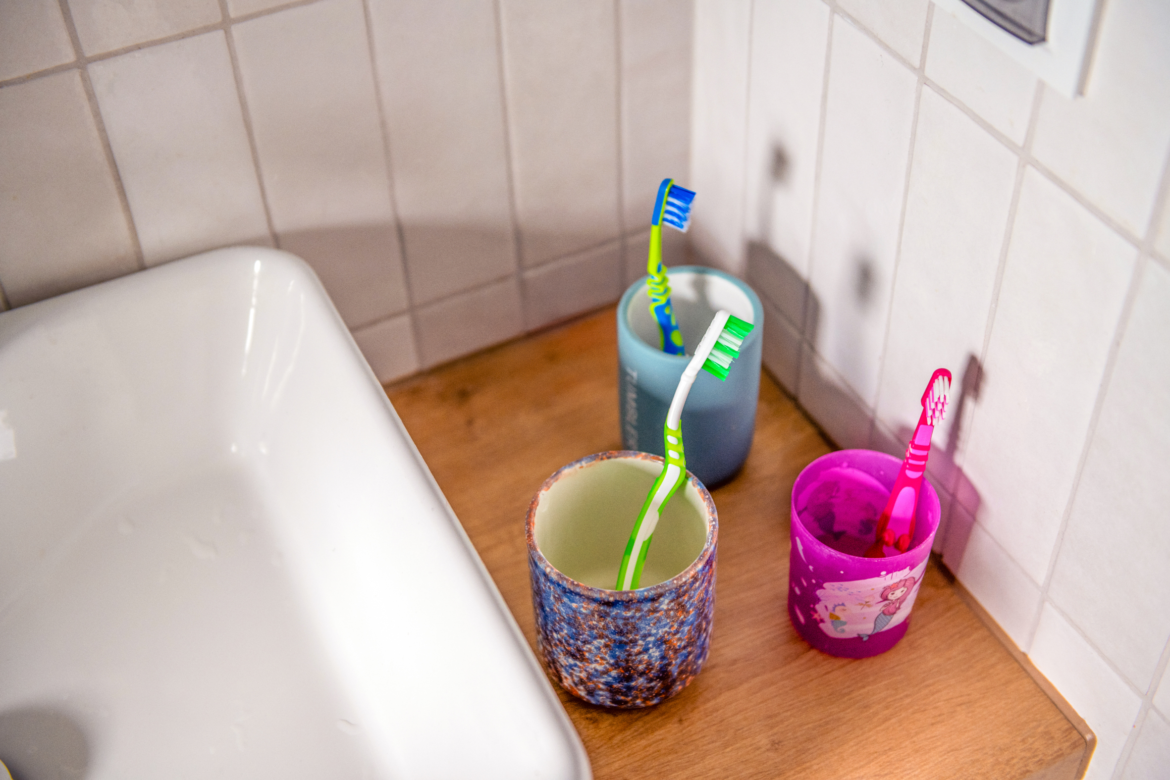 Toothbrushes kept in separate mugs next to bathroom sink