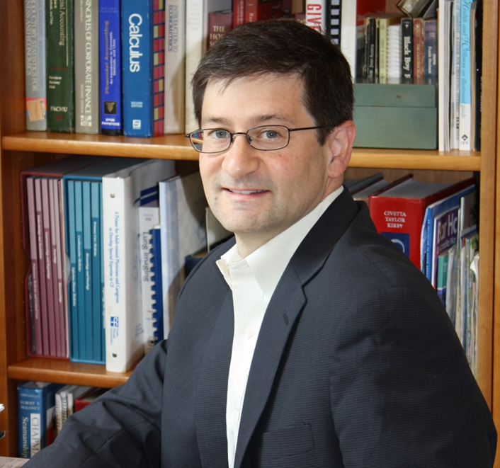 Man in suit sitting in front of bookshelf