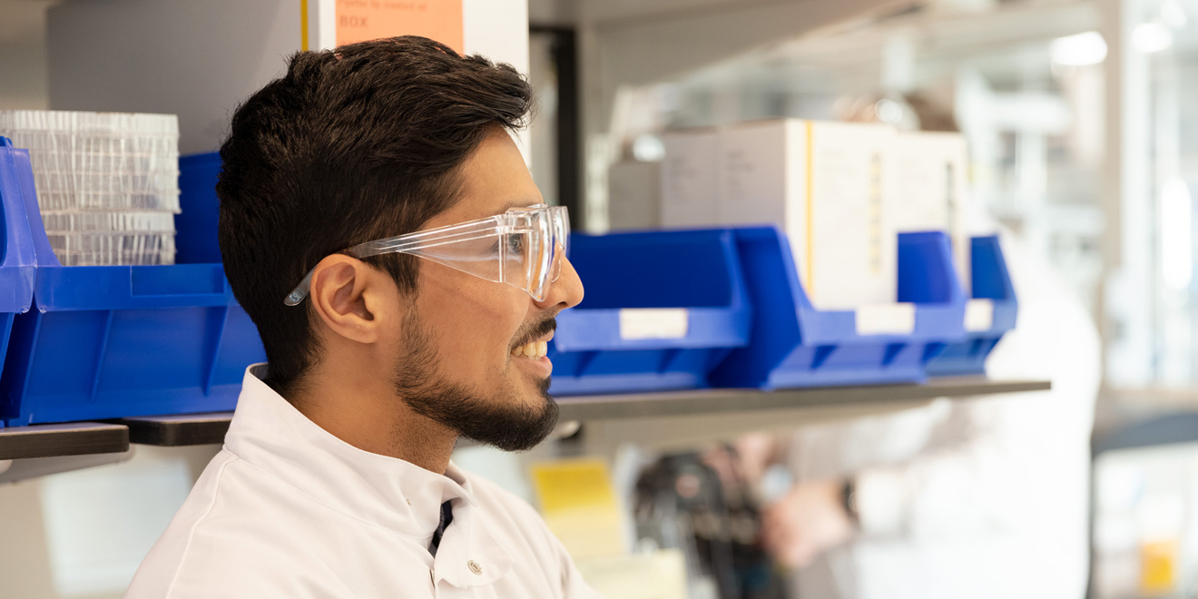 Man in labcoat and protective goggles smiling