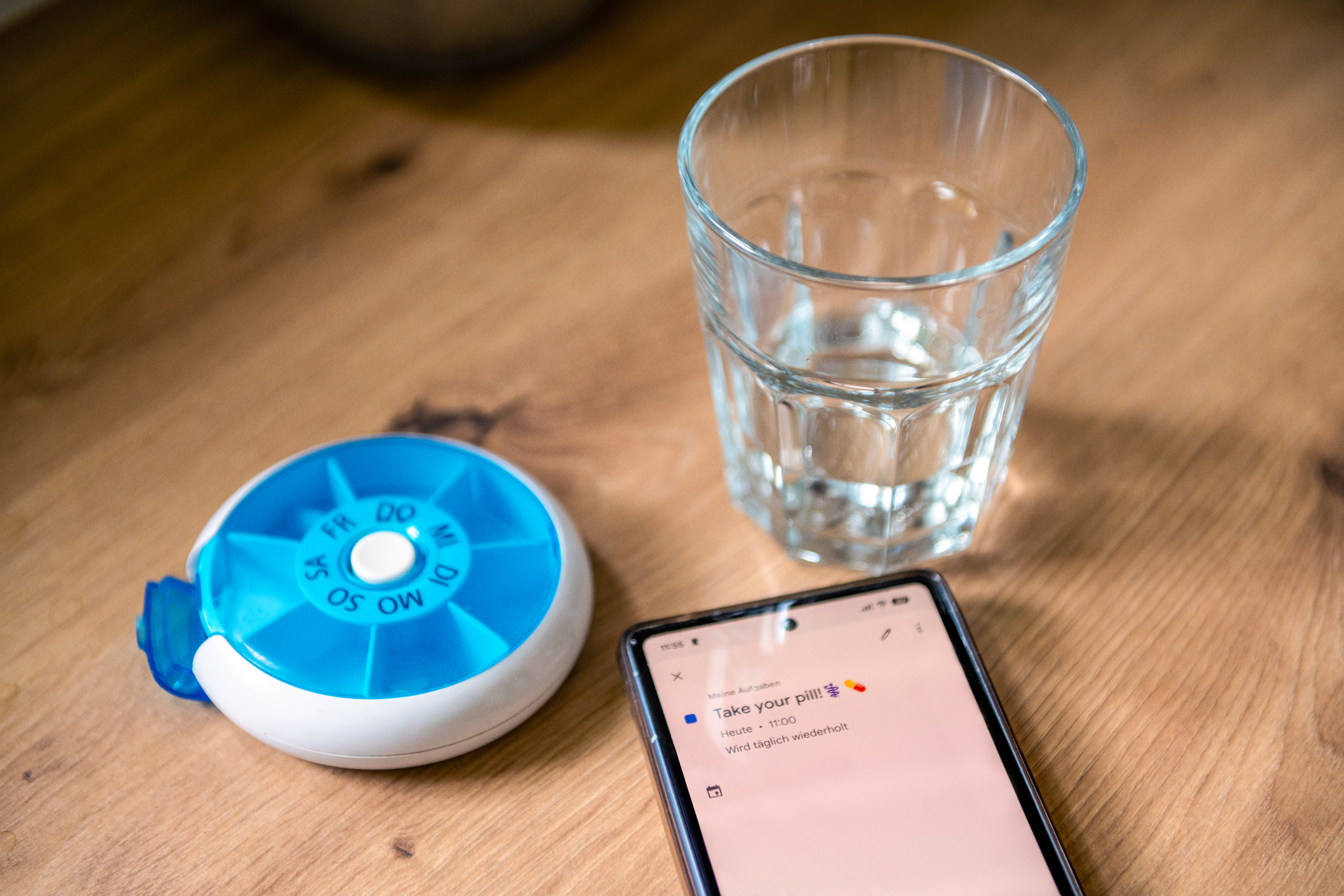 Phone with a reminder on daily medication, a pill box, and a glass of water 