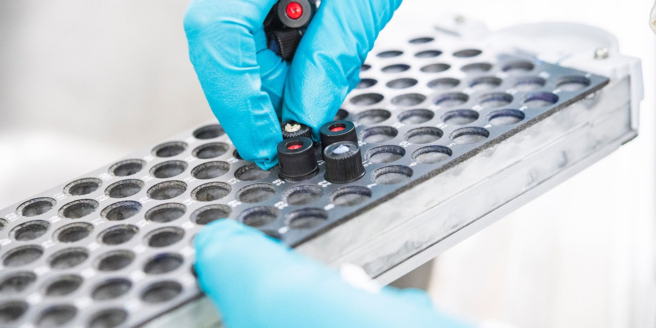 scientist with blue gloves placing testing tubes on a rack
