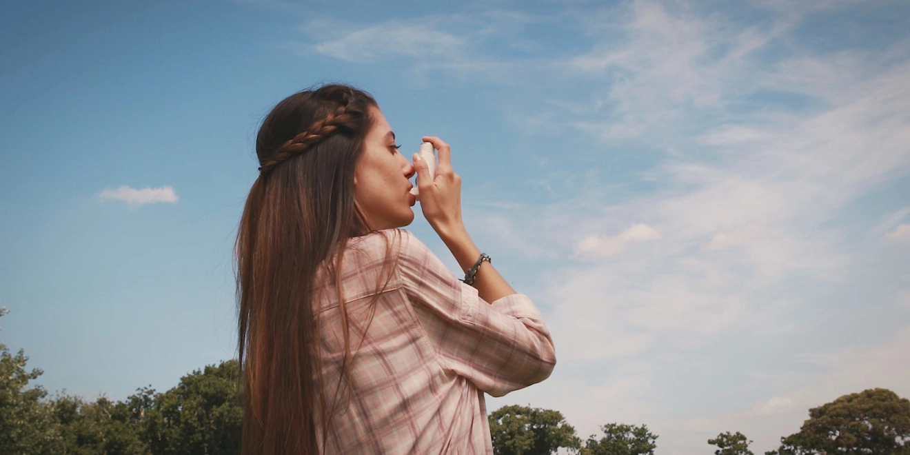 A woman outside using an inhaler