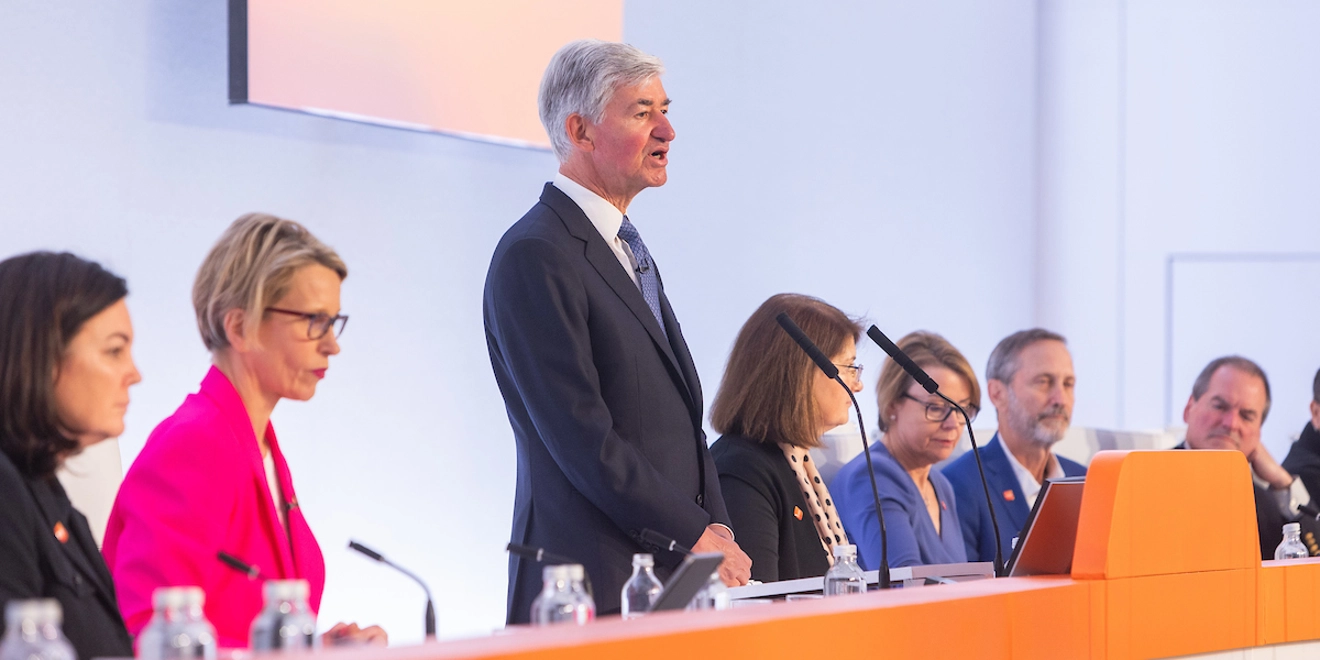Jon Symonds, standing at podium, flanked by GSK leadership, Board Directors, all seated