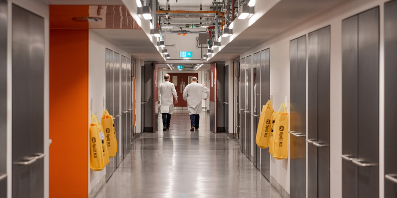 Two men in labcoats walking down long hallway